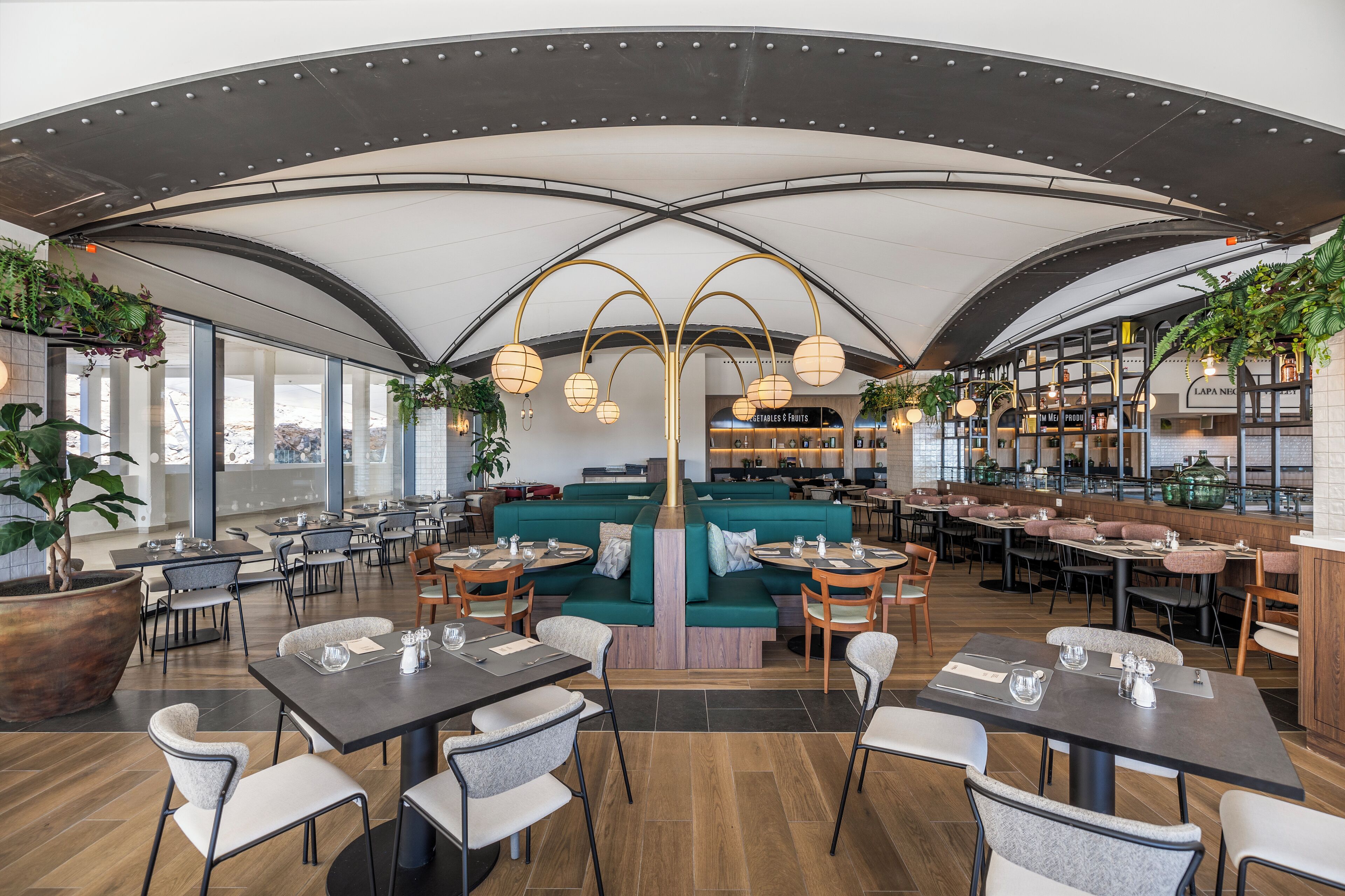 A modern restaurant with a high ceiling, green seating, and a bar area.