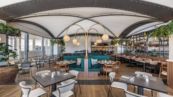 A modern restaurant with a high ceiling, green seating, and a bar area.