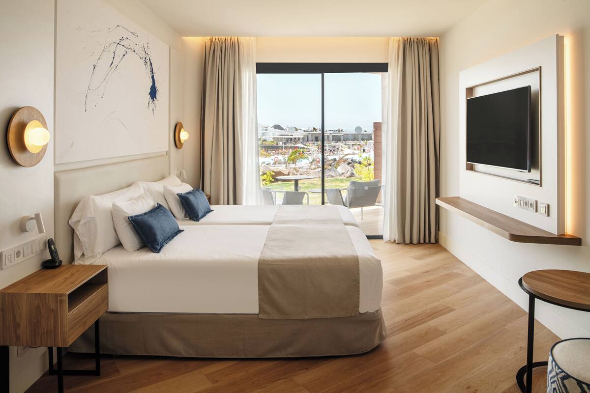 Ein Hotelzimmer mit zwei Betten, einem Fernseher, einem Schreibtisch und einem Balkon mit Blick.