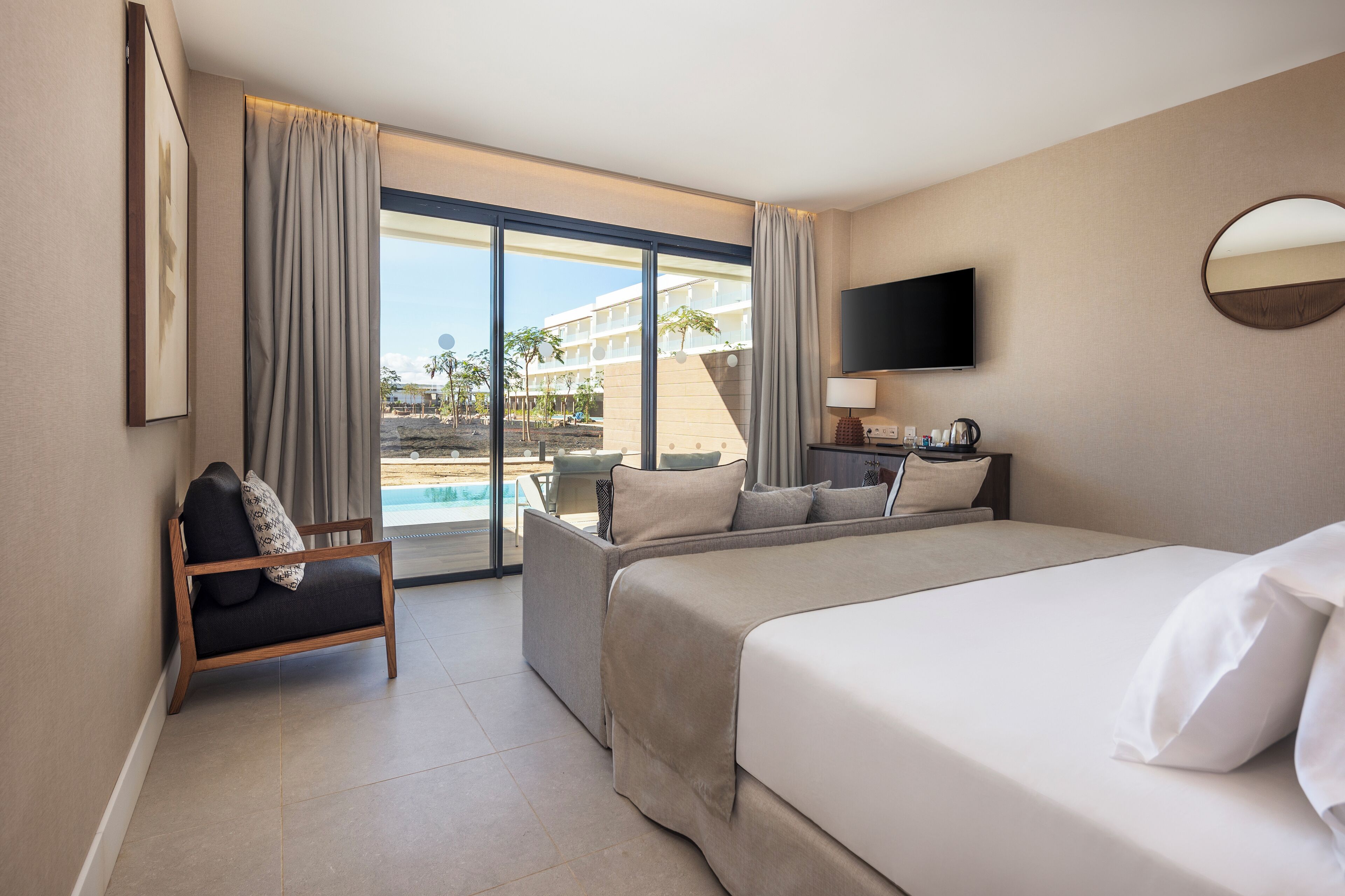 A hotel room with a large bed, a sofa, a TV, and a view of a pool and building.
