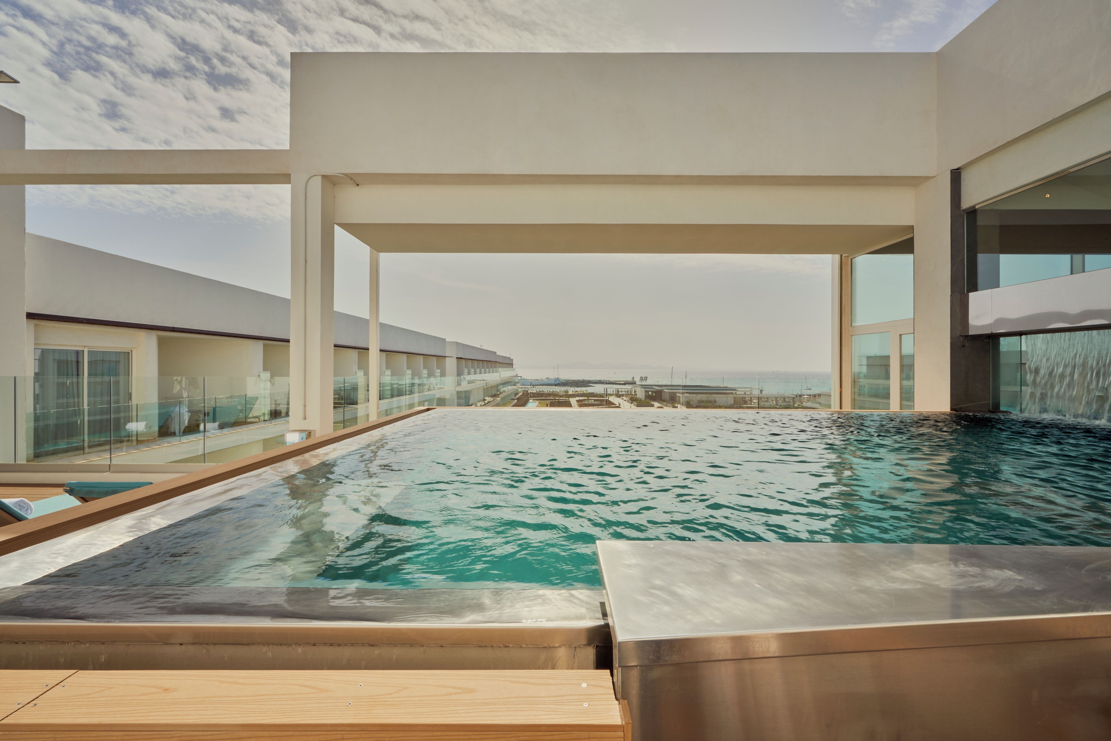 Una piscina infinita moderna con vistas despejadas al océano, rodeada de barandales de vidrio y arquitectura minimalista.