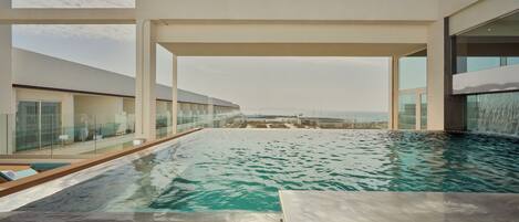 Une piscine à débordement moderne offrant une vue dégagée sur l’océan, entourée de rampes de verre et dotée d’une architecture minimaliste.