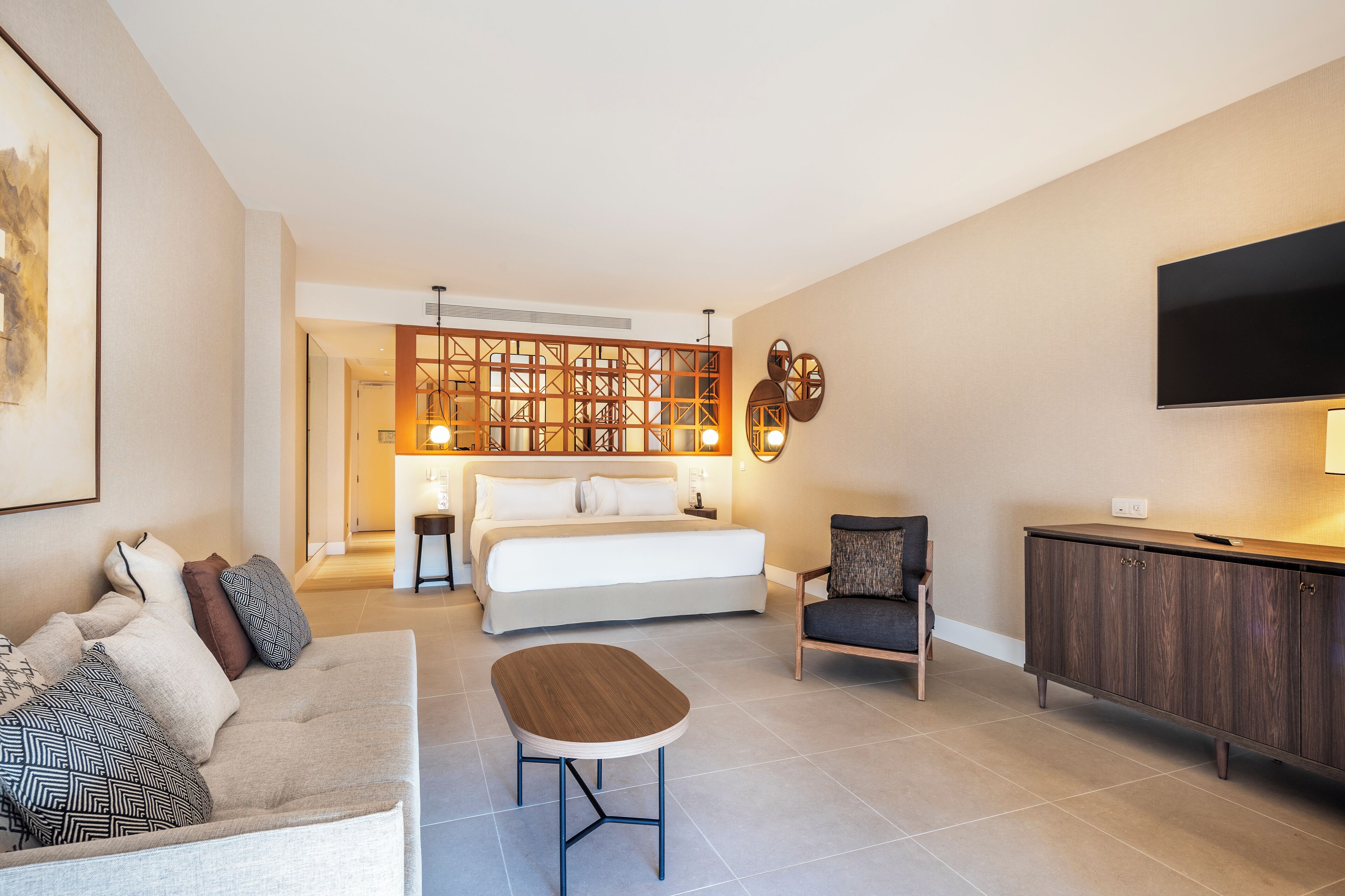 Una habitación de hotel moderna con una cama grande, un sofá, una mesita, un armario y un televisor montado en la pared.
