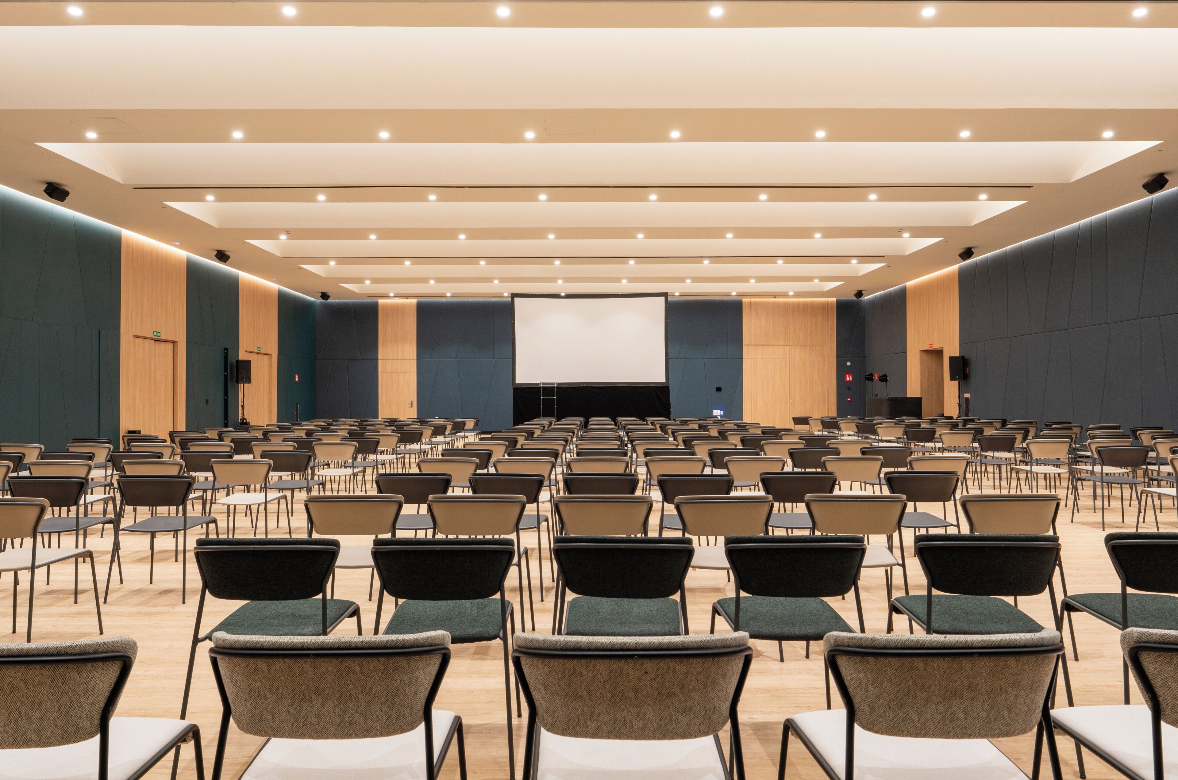 Un amplio salón de conferencias con filas de sillas y una gran pantalla al frente.