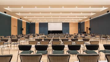 Un amplio salón de conferencias con filas de sillas y una gran pantalla al frente.
