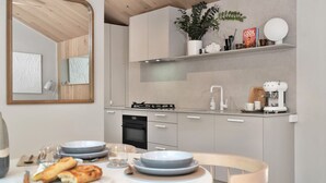 Une cuisine moderne avec des meubles blancs, une cuisinière à gaz, une machine à café et un coin repas avec une table mise pour deux personnes.