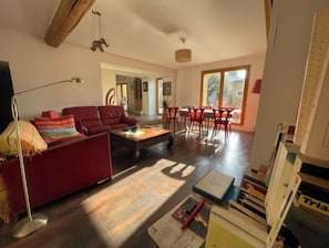 A spacious living room with a red sofa, a coffee table, and a dining area with red chairs.