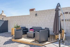 Relax on the patio with comfortable sofas and a coffee table, surrounded by a wooden deck and a brick wall.