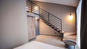 A modern bedroom with a bed, a small round table, a wardrobe, and a staircase with a railing. - Teghenis Resort (Tsaghkadzor)