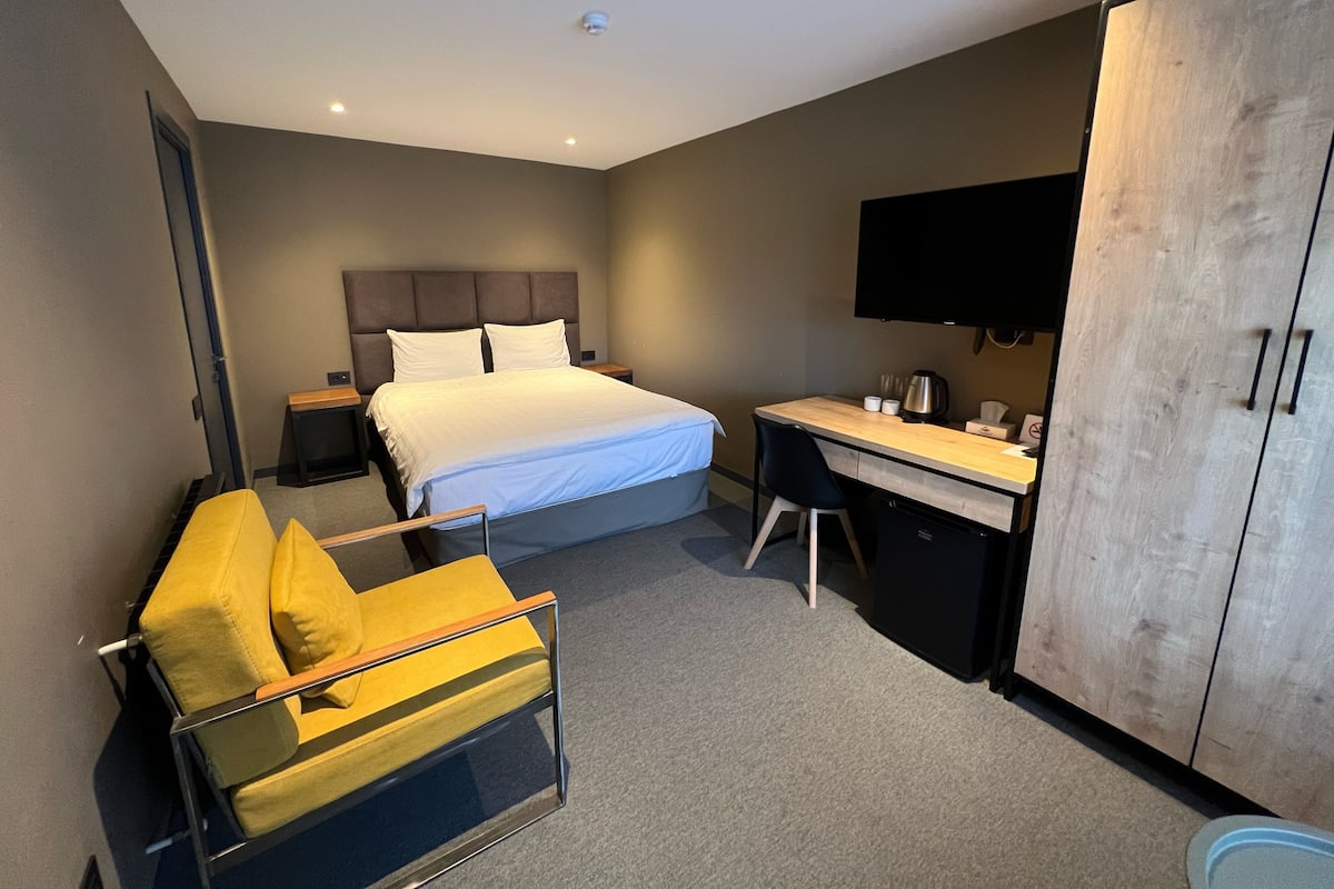 A modern hotel room with a bed, a desk, a chair, a wardrobe, and a television.