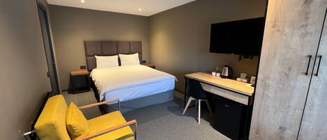 A modern hotel room with a bed, a desk, a chair, a wardrobe, and a television.
