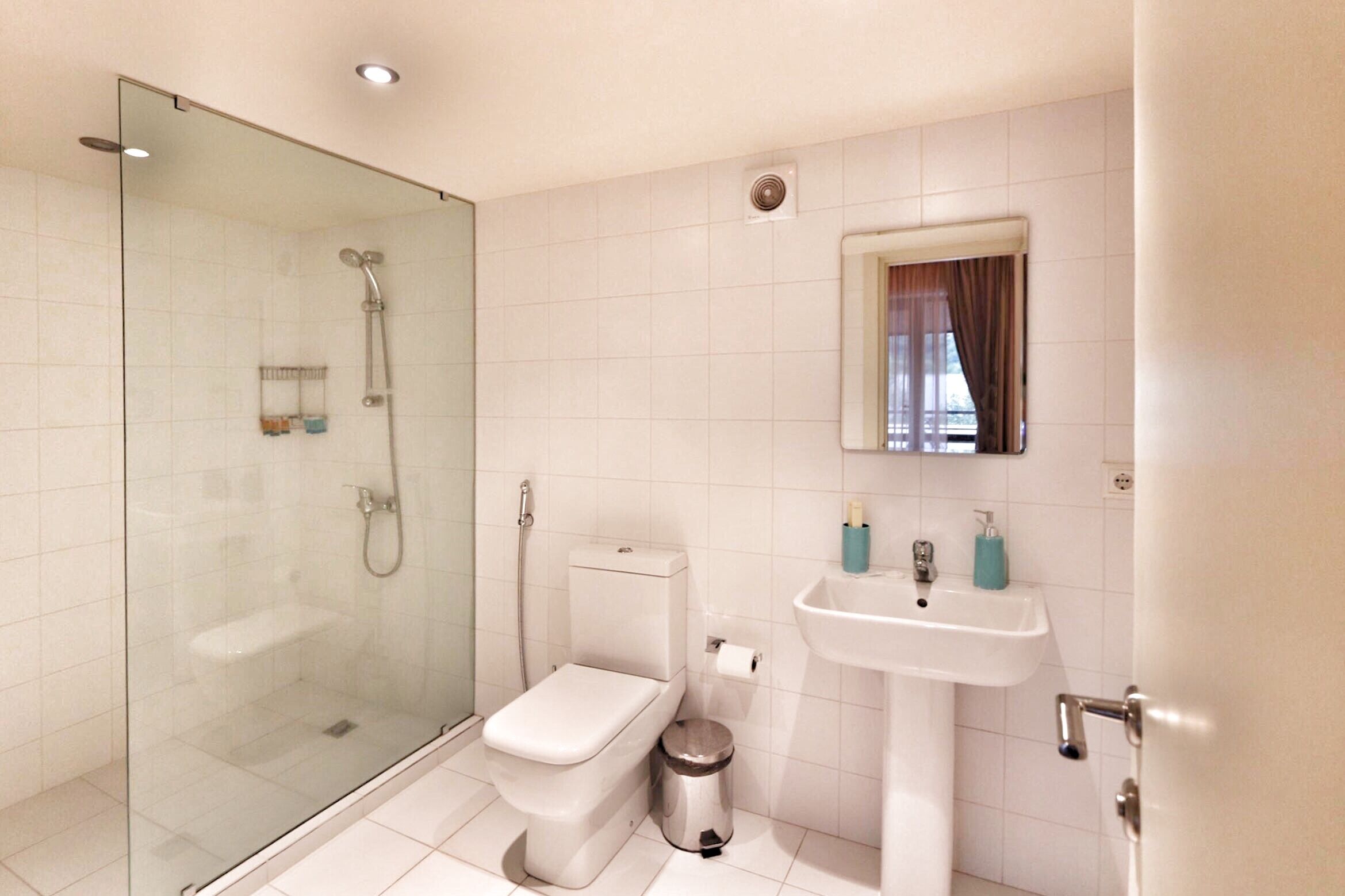 Un baño moderno con ducha envuelta en vidrio, inodoro, lavamanos y espejo.