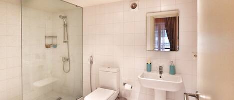 Un baño moderno con ducha envuelta en vidrio, inodoro, lavamanos y espejo.
