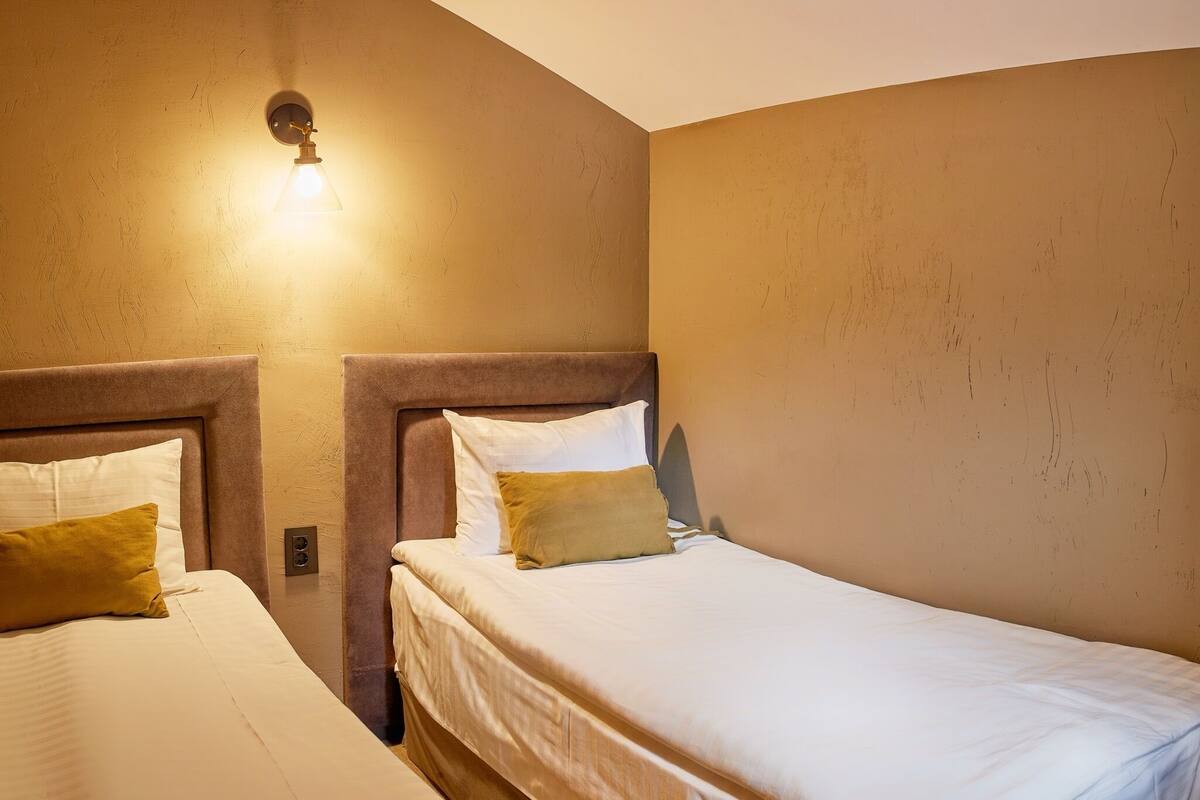 A bedroom with two beds, each with a headboard and pillows. There is a wall-mounted light fixture above the beds.
