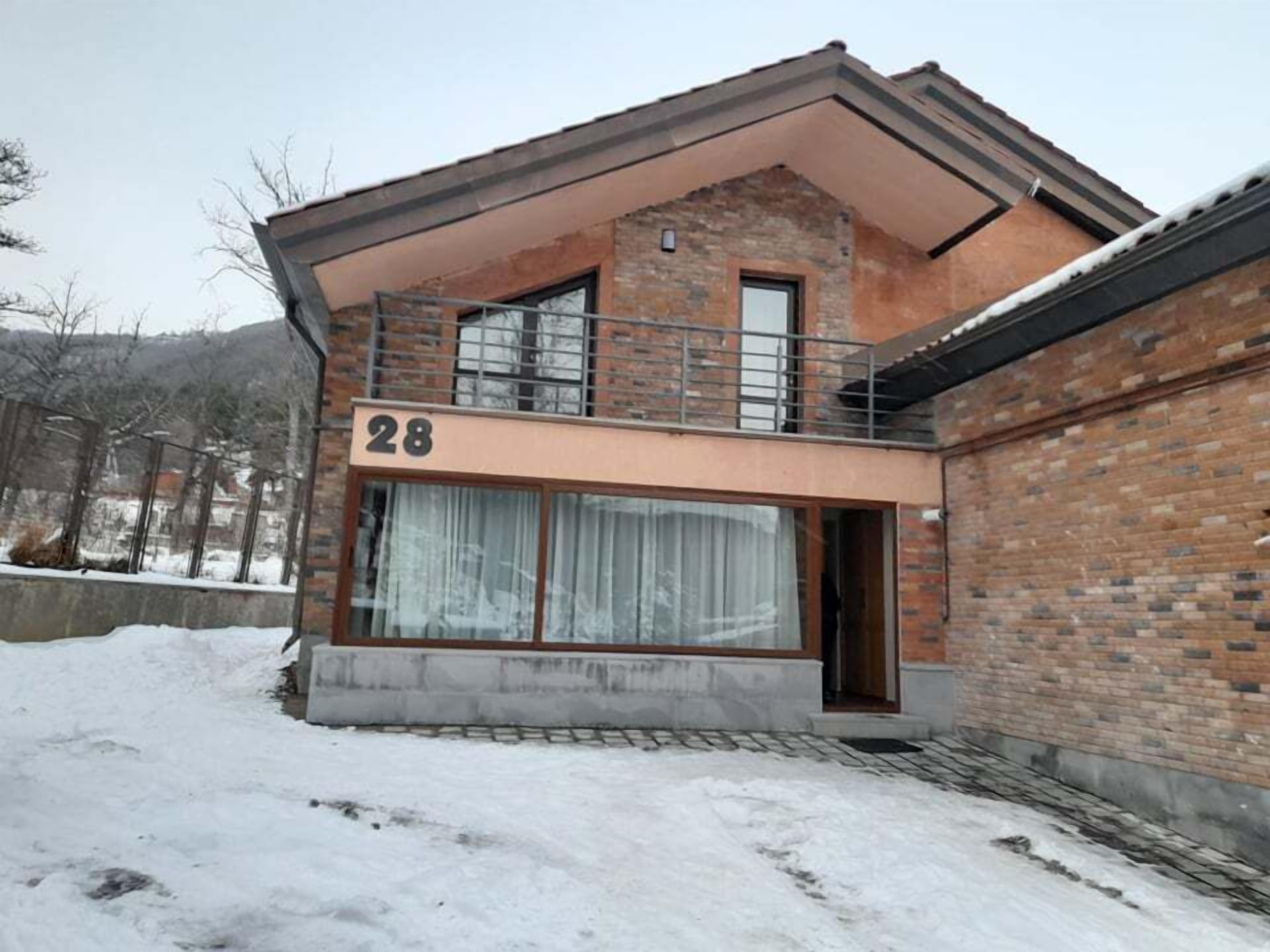 A two-story house with a balcony, number 28, and a large window with curtains.