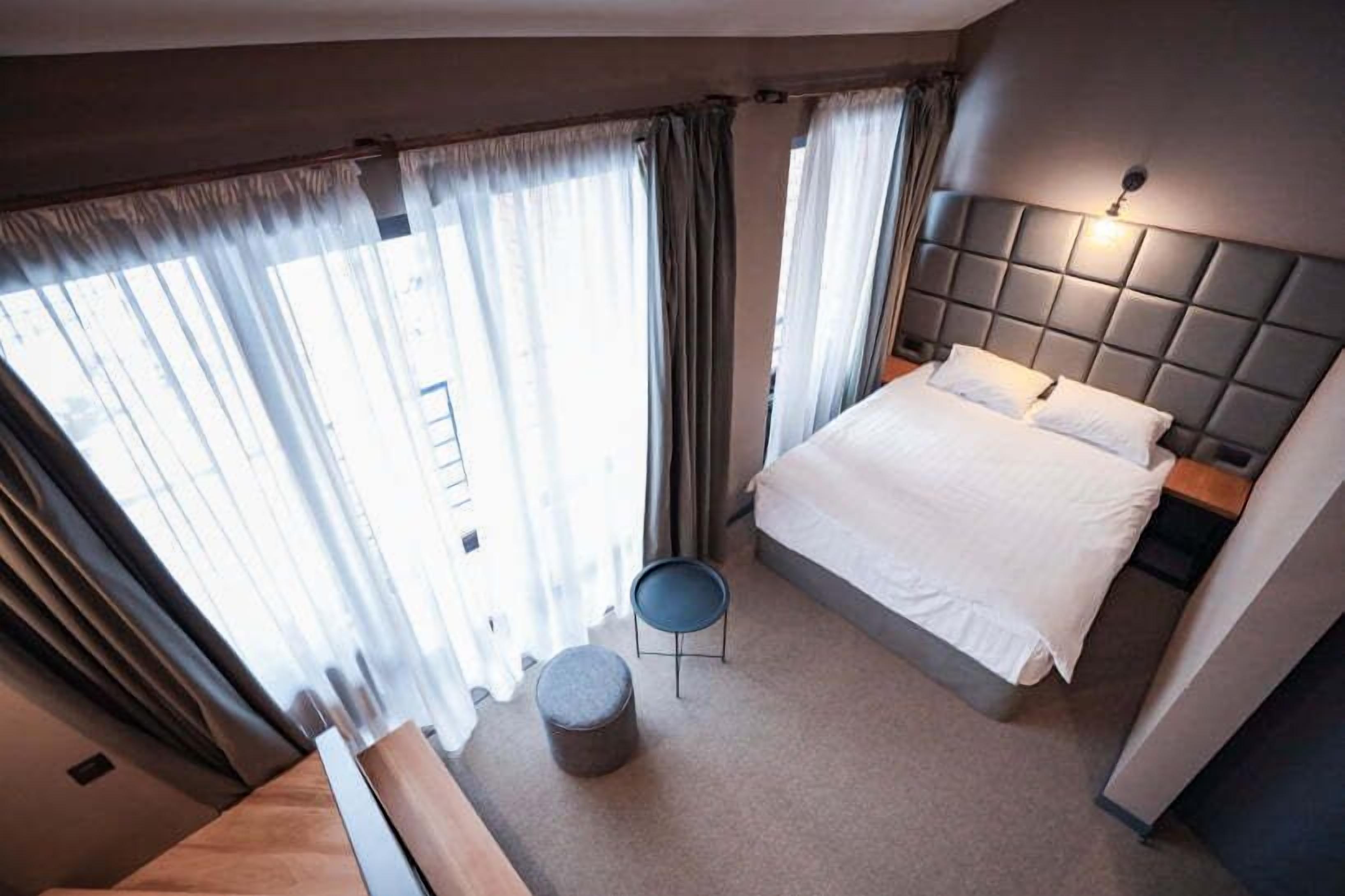 A hotel room with a large bed, a small round table, and a view of the outdoors through sheer curtains.