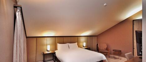 A hotel room with a large bed, bedside tables, a chair, a small table, and a TV.