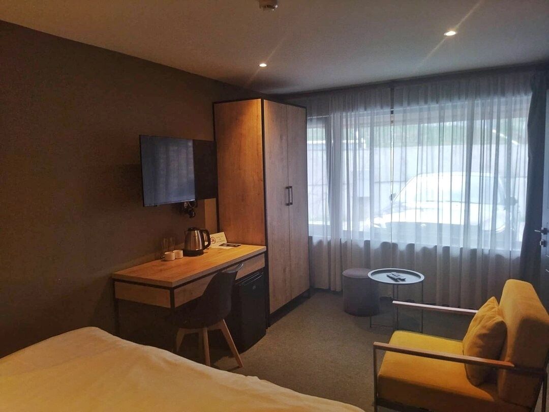 Habitació d'hotel amb un llit, una taula de nit amb cadira, una televisió, una taula rodona petita i una finestra amb cortines.