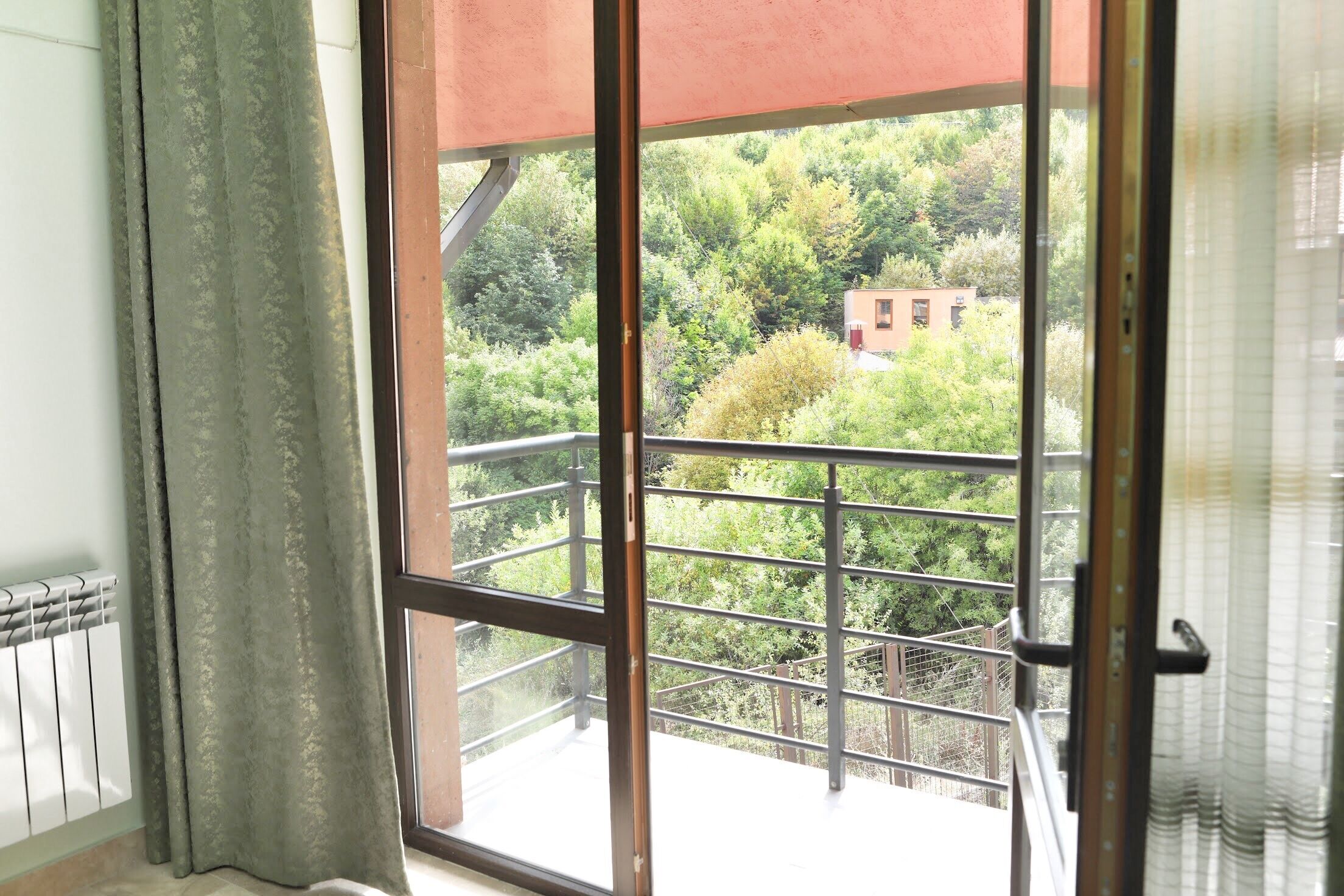 A balcony with a metal railing overlooking a green landscape with trees and a building.