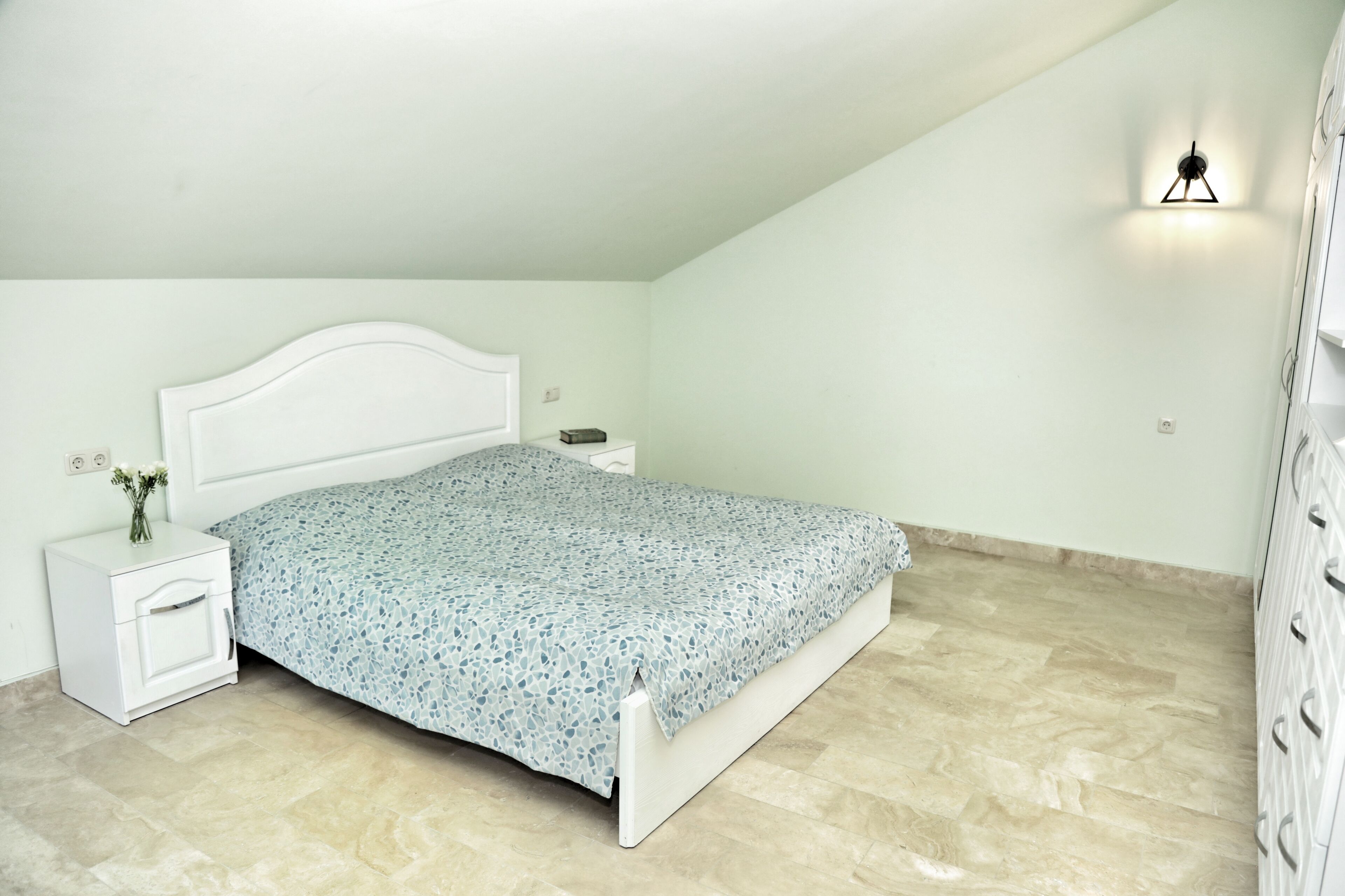 A bedroom with a bed, nightstand, and wall-mounted light fixture.