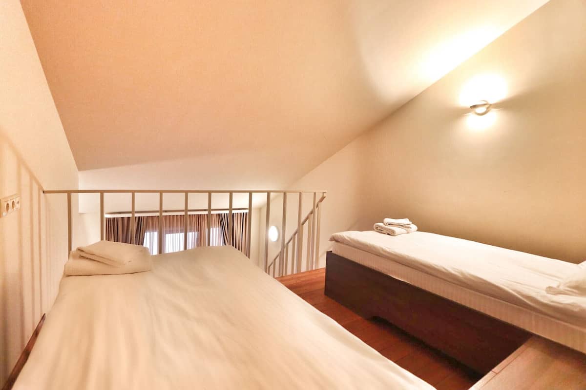 A small, cozy room with a single bed, a bedside table, and a wall-mounted light fixture.