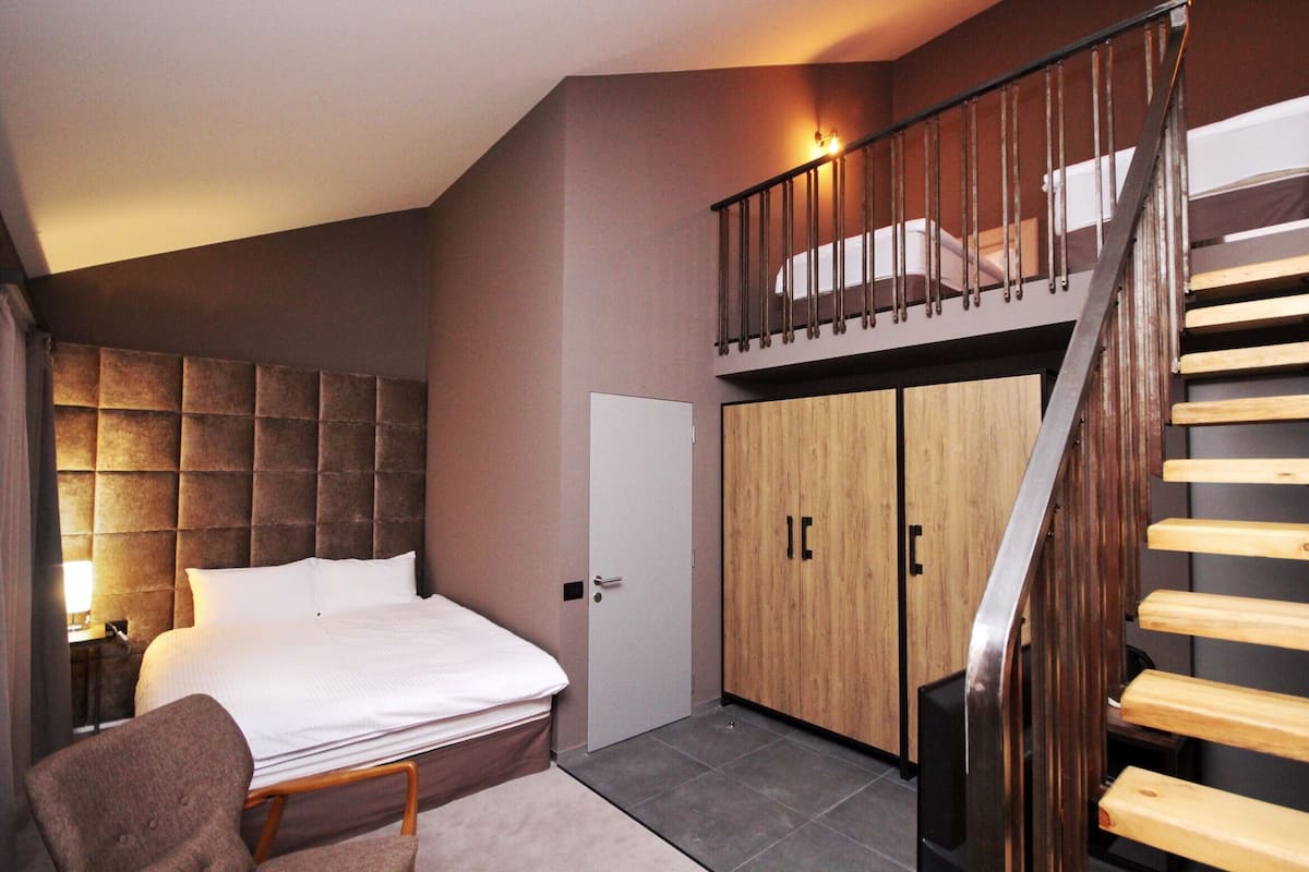 A bedroom with a bed, a chair, a wardrobe, and a staircase.