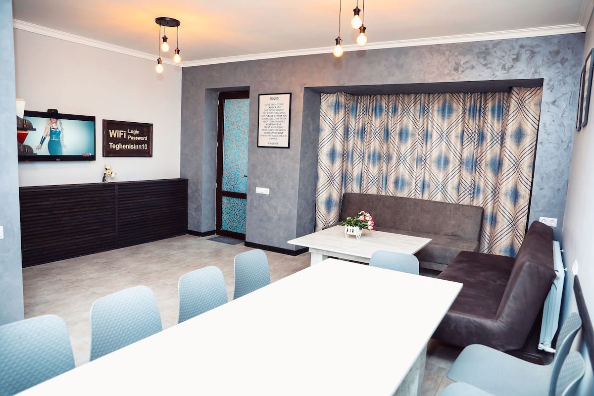 A modern living room with a white table, blue chairs, a brown sofa, and a patterned curtain.