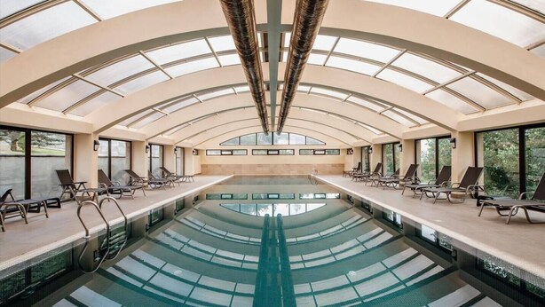 A large indoor swimming pool with a glass ceiling, lounge chairs, and a view of the outdoors. - Teghenis Resort (Tsaghkadzor)