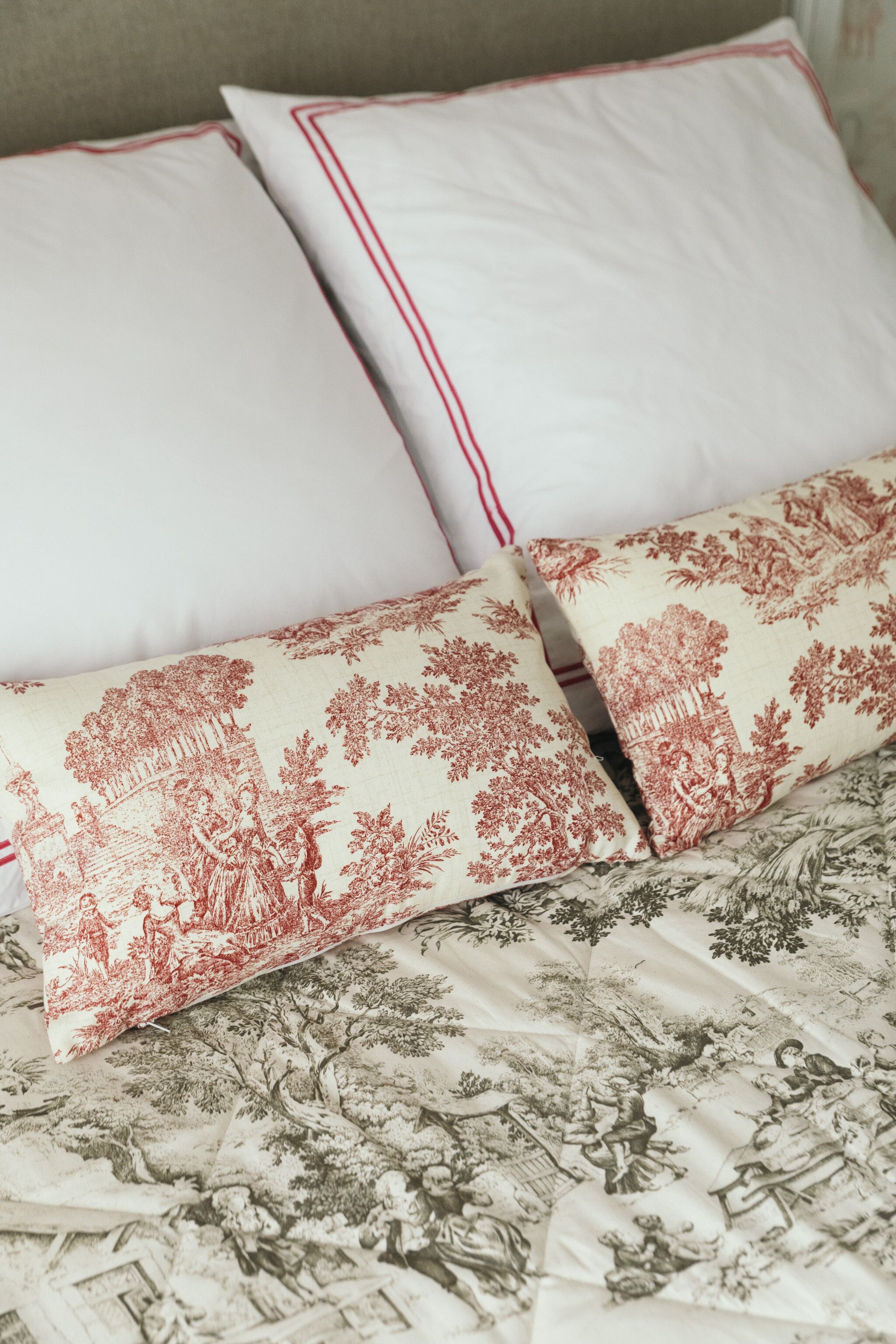 A bed with floral bedding and two pillows, one plain and one with a red pattern.