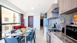 A modern kitchen with a marble countertop, a built-in oven, and a dining area with a glass table and chairs. - Islet Seafront Apartment Corner Terrace (St. Paul's Bay)