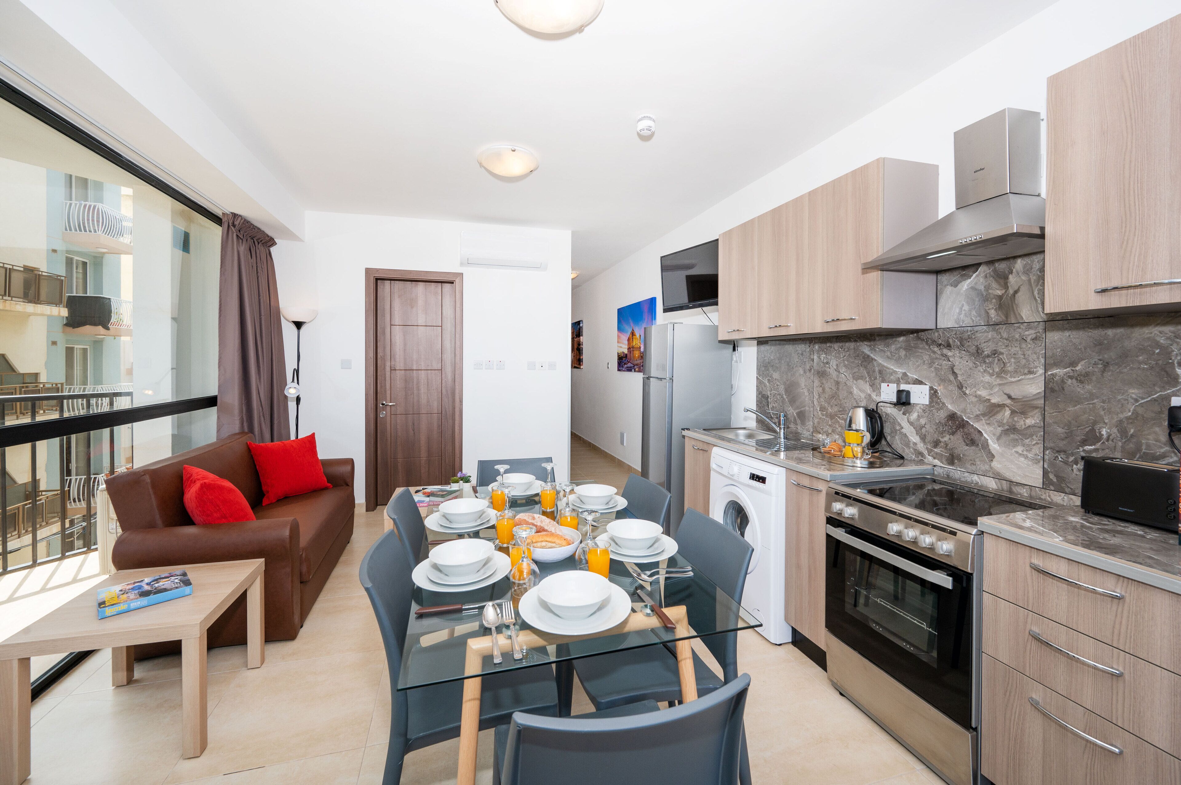 A modern apartment with a dining area, a sofa, a kitchen with a stove, and a washing machine.