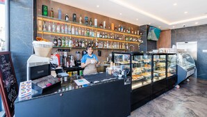 A modern bar area with a coffee machine, shelves of liquor bottles, and a display case with pastries. - Islet Seafront Apartment Corner Terrace (St. Paul's Bay)