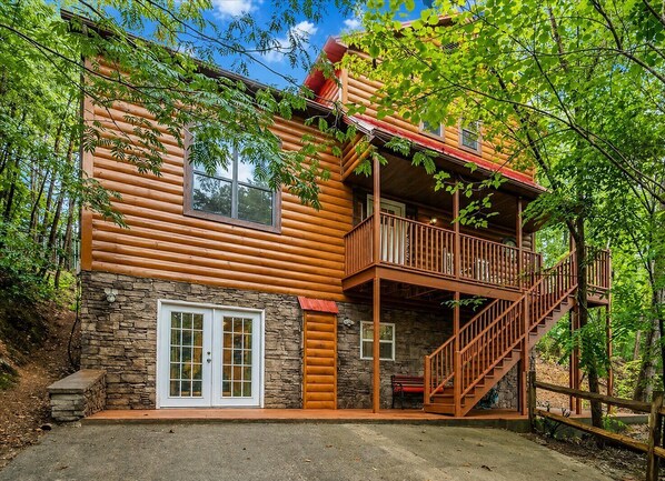 A log cabin with a stone foundation, a balcony, and a staircase leading to the upper level. - Enchanted Memories- Less than a mile to Pigeon Forge! Home Theater! (Pigeon Forge)