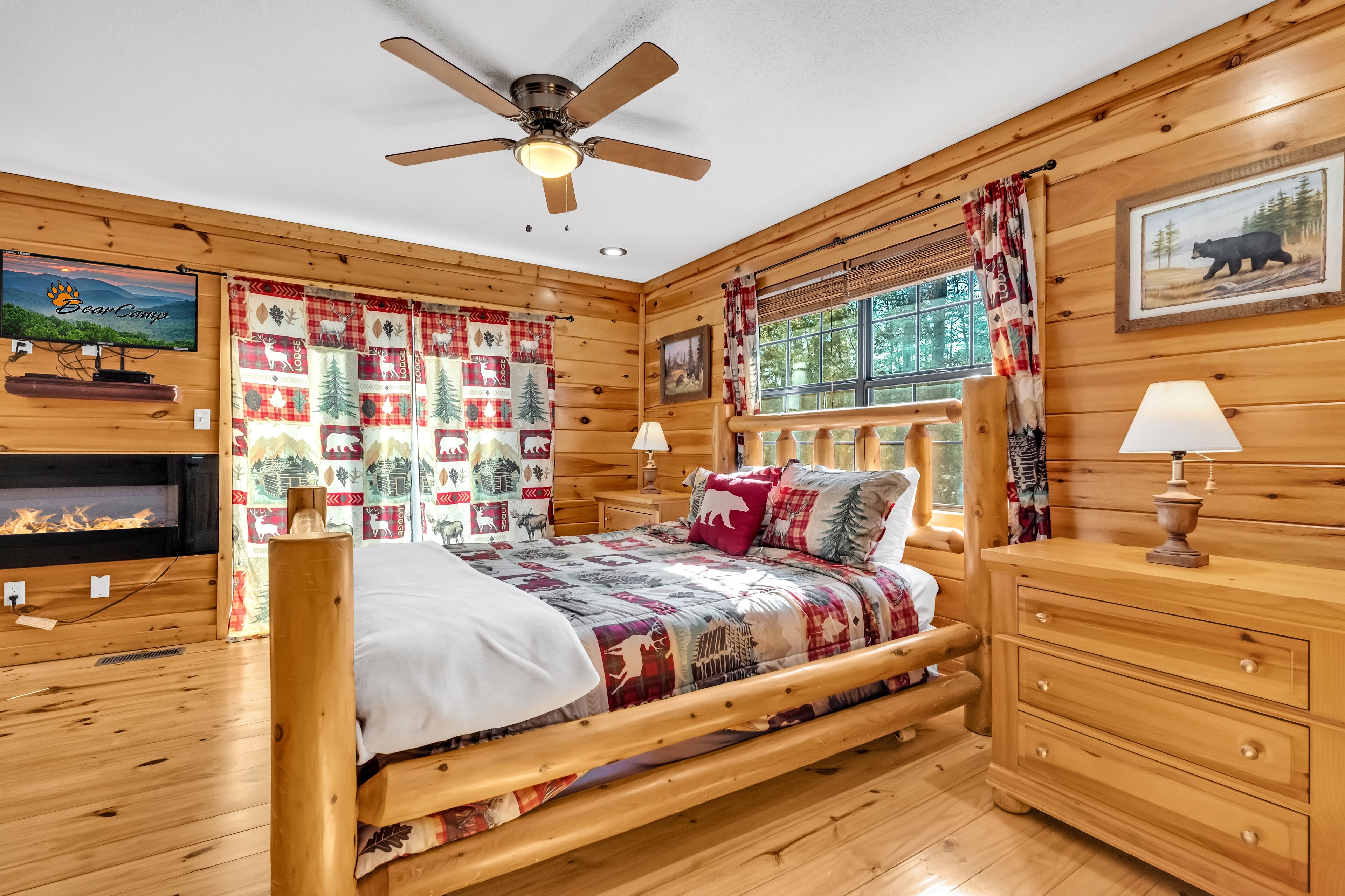 Une chambre confortable, aménagée dans le style d’un chalet, avec un lit en bois, un ventilateur de plafond, une cheminée et une fenêtre avec des rideaux.