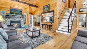 A cozy cabin interior with a fireplace, wooden walls, a staircase, and a dining area. - Enchanted Memories- Less than a mile to Pigeon Forge!  Home Theater! (Pigeon Forge)