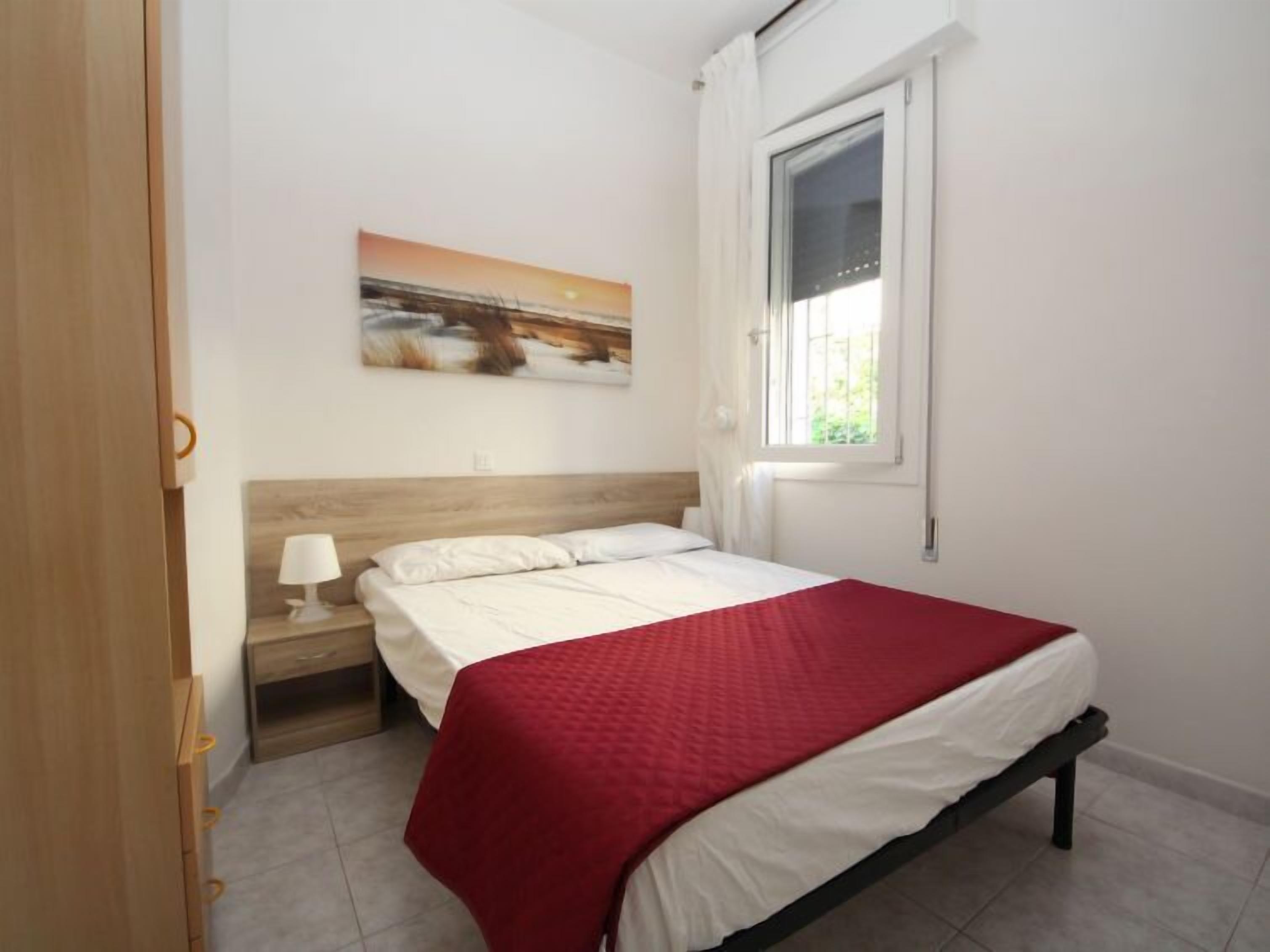 Une chambre à coucher avec un lit, une table de chevet, une lampe, une fenêtre et un tableau au mur.