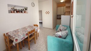 A compact living space with a dining table, a sofa, a kitchen area, and a clock on the wall.