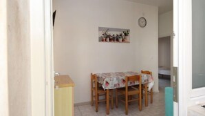 A dining area with a table covered by a patterned tablecloth, wooden chairs, a clock on the wall, and a small cabinet.