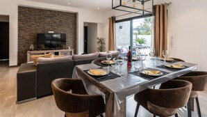 Un espace repas moderne avec une table en verre, des chaises marron et un téléviseur en arrière-plan.