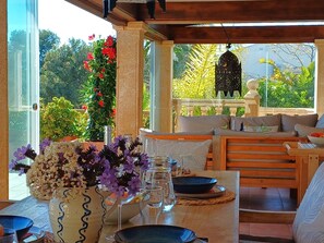 A dining area with a table set for two, a vase with flowers, and a view of greenery outside. - Villa Lantana by Interhome (Jávea)