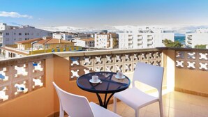 Un balcon avec une table et des chaises, donnant sur un paysage urbain avec des immeubles et une vue sur la mer.