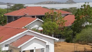A residential area with houses featuring red roofs and white walls, surrounded by greenery and a distant body of water. - Sandai resort (Marigat)
