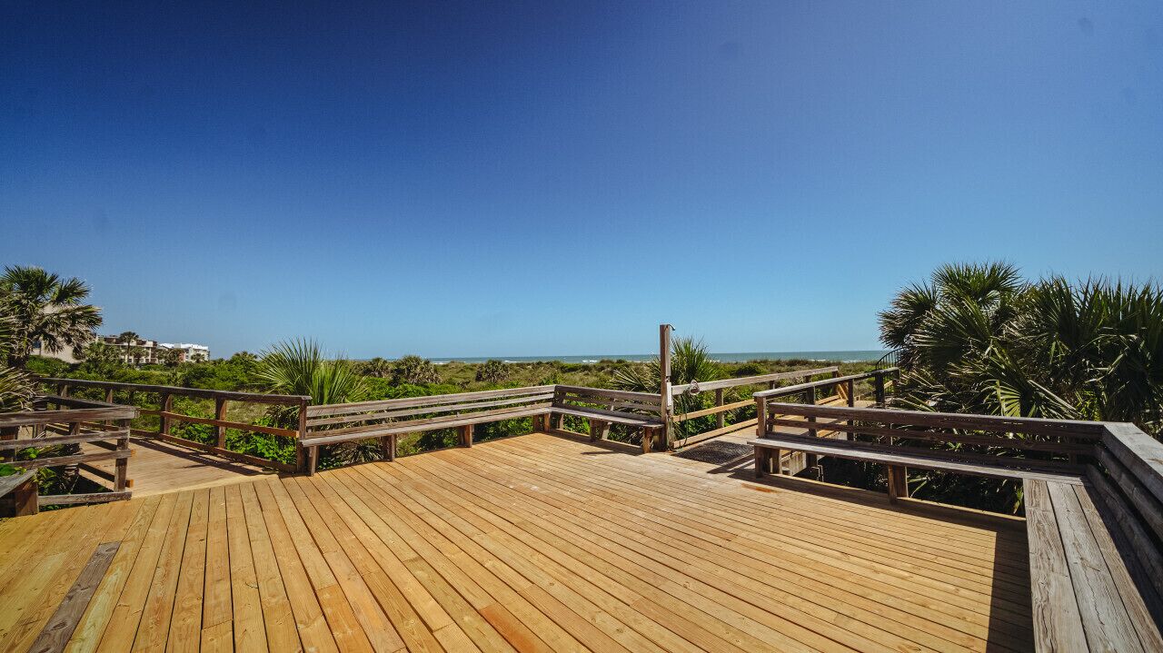 A wooden deck with benches and railings overlooking a beach and ocean.