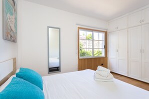 A bedroom with a bed, a window, a wardrobe, and a painting on the wall.