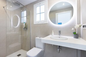 A modern bathroom with a glass-enclosed shower, a toilet, a sink with a mirror, and a potted orchid.