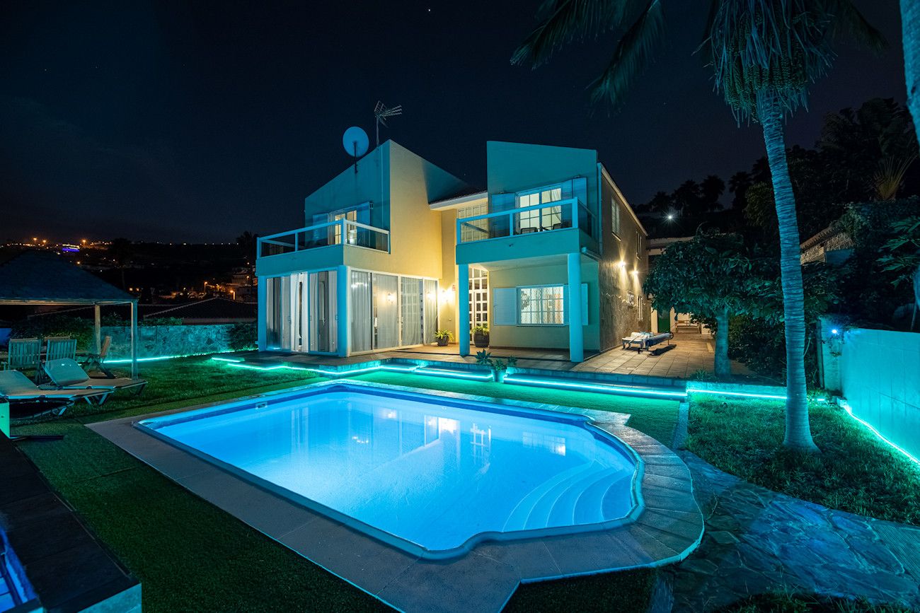 Une maison moderne à deux étages, dotée d’une piscine, d’un éclairage extérieur et offrant une vue sur le paysage environnant.