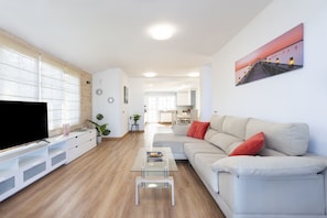 A modern living room with a flat-screen TV, a glass coffee table, a beige sofa with red cushions, and a painting on the wall. - Fantastic home with amazing sea views (El Sauzal)