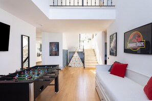 Uma sala de estar moderna com uma mesa de futebol, um sofá com almofadas vermelhas e uma escada que leva a um andar superior.