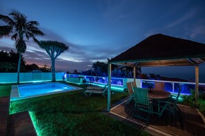 Un área de piscina con zona de estar cubierta y una pérgola.