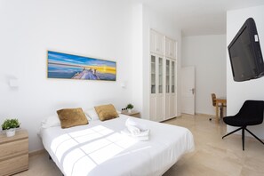Quarto de hotel moderno com uma cama grande, uma mesa de trabalho, uma cadeira, uma televisão e um quadro na parede.
